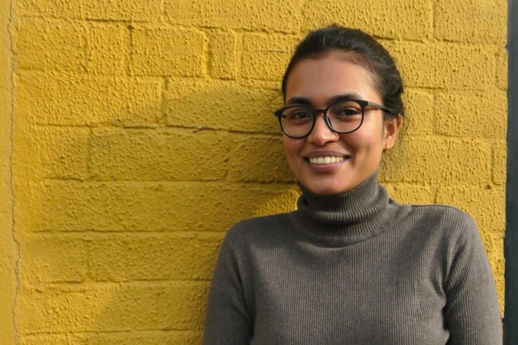 Athira, our new planning assistant, standing against a yellow wall