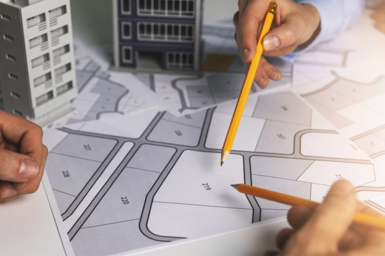 there is a map of a neighbourhood plan on a table, with 3D models of buildings placed over the top, there are three hands from three different people, two are holding pencils and it gives the impression of everyone working together