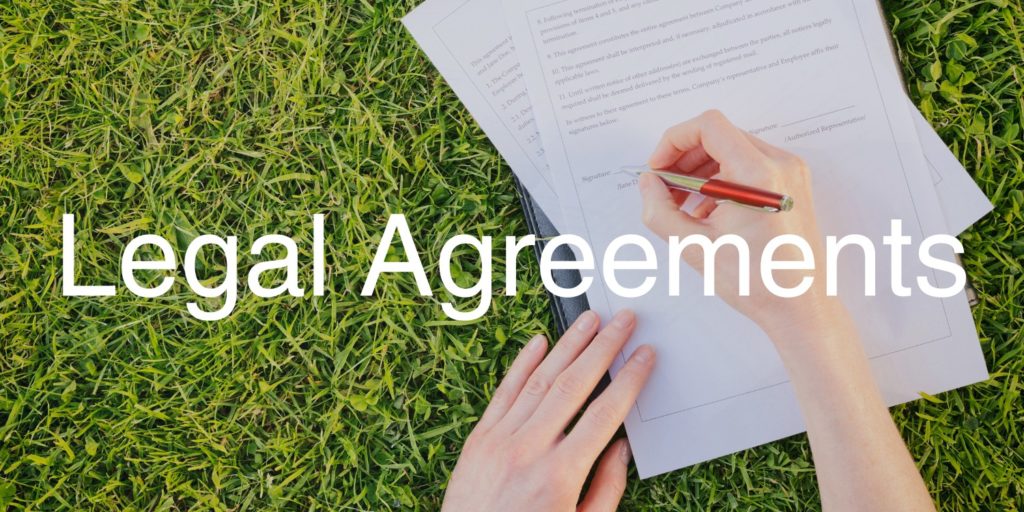 Someone is filling out a legal document in a folder, with the text 'legal agreements' at the forefront of the image
